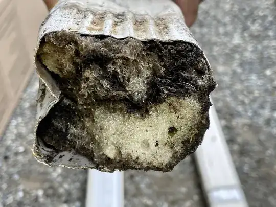 Downspout clogged by brown/black and beige foam-like substance