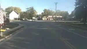 A street-level picture of a residential intersection, showing a sidewalk on the left with lowered curb ramp, and sidewalk on the right separated with a grassy verge.