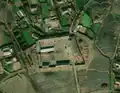 4/6 Farmyard (landuse=farmyard) composed of long buildings surrounded by a fence dotted with hay piles, near a road very close to a village (Maxar satellite imagery).
